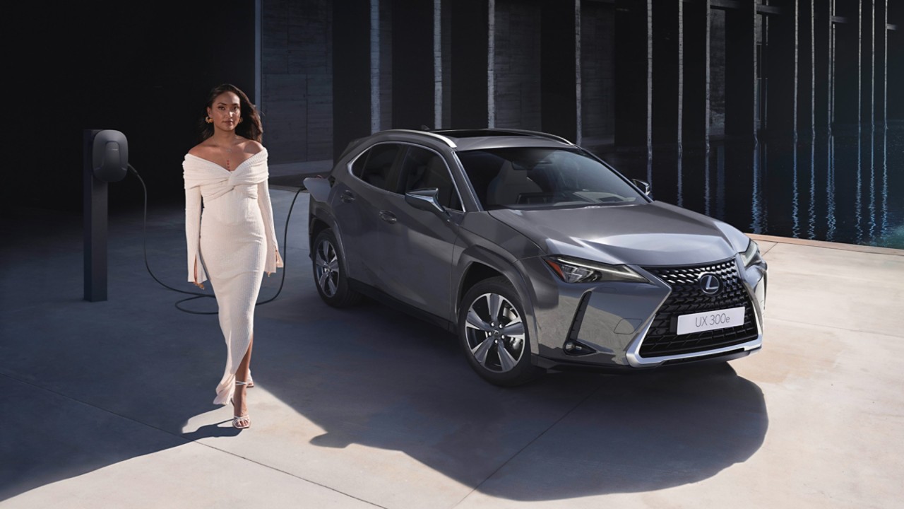 Жена в бяла рокля стояща до зареждащ се автомобил Lexus UX 300e